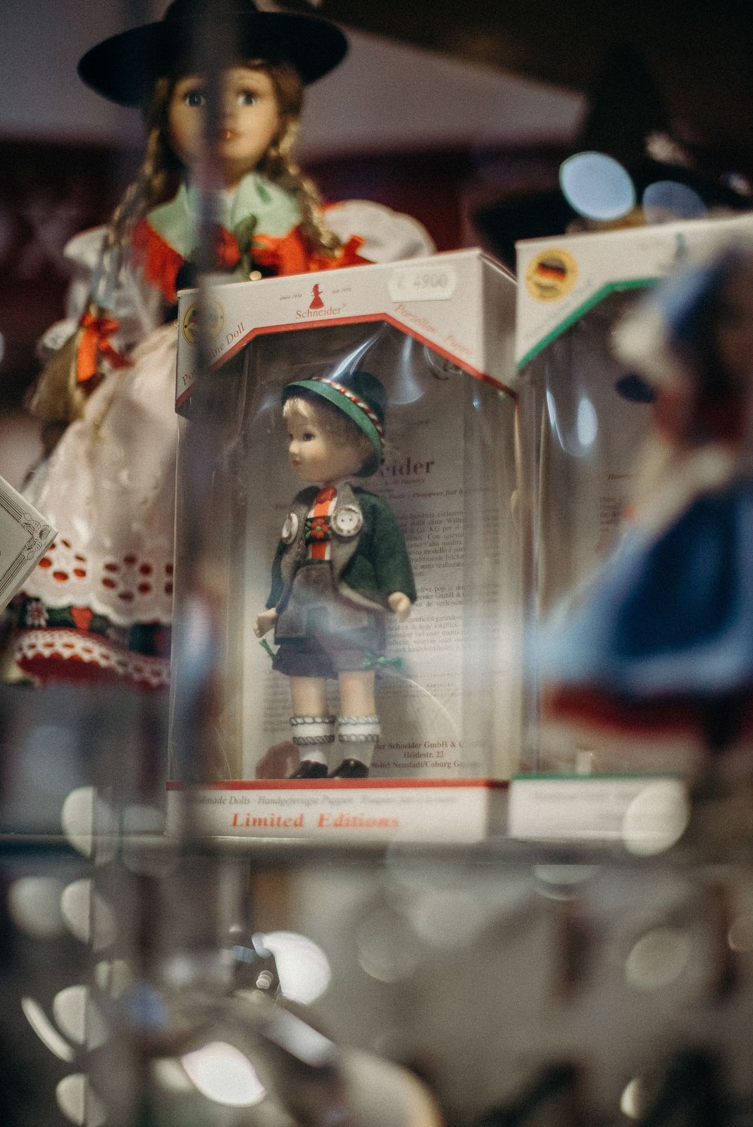 Boxed porcelain doll in alpine costume with green felt hat and jacket, displayed inside a glass cabinet